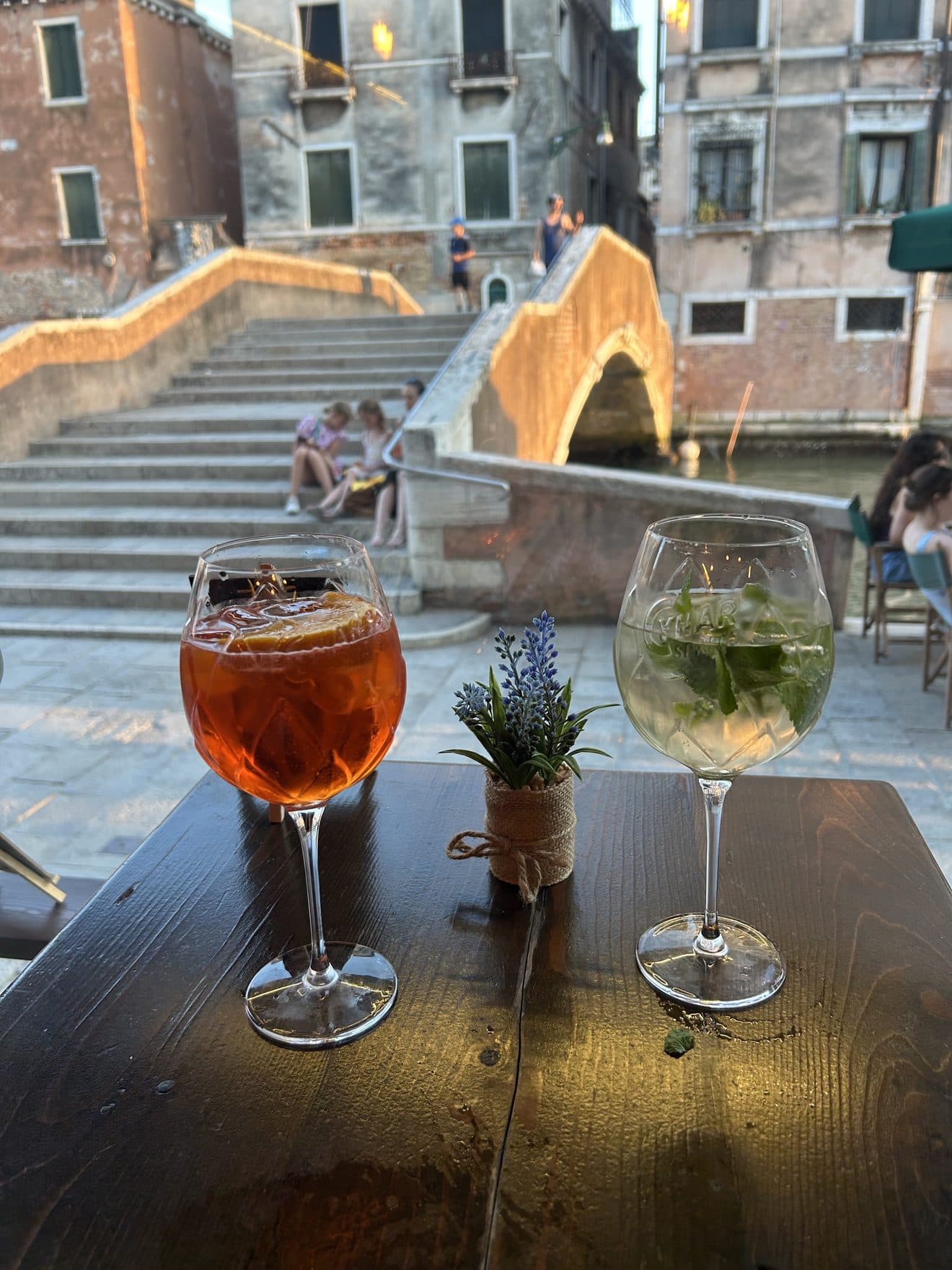 An Aperol spritz and a long drink with fresh mint on a table facing the bridge over the canal