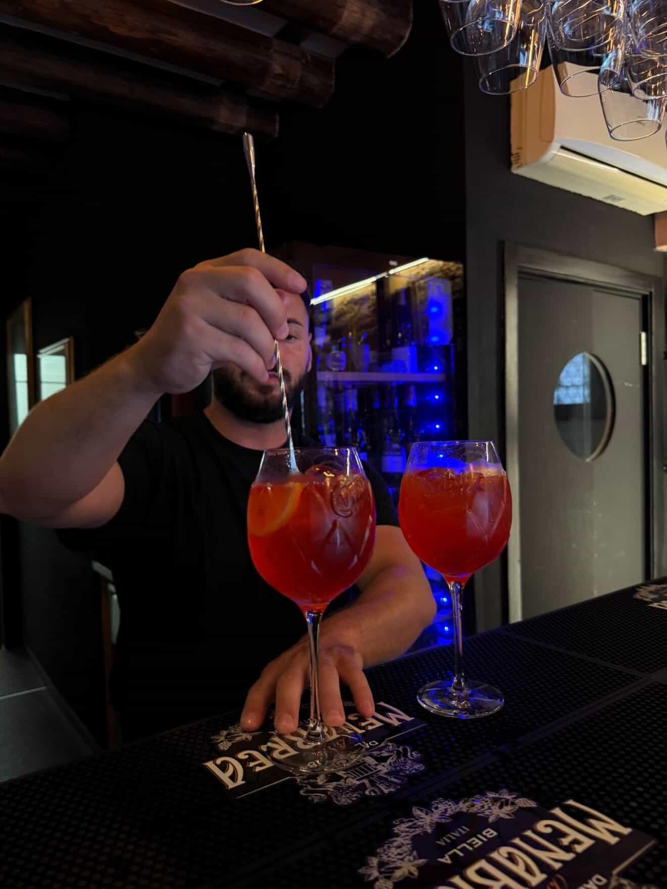 Bartender stirring two spritz cocktails by candlelight