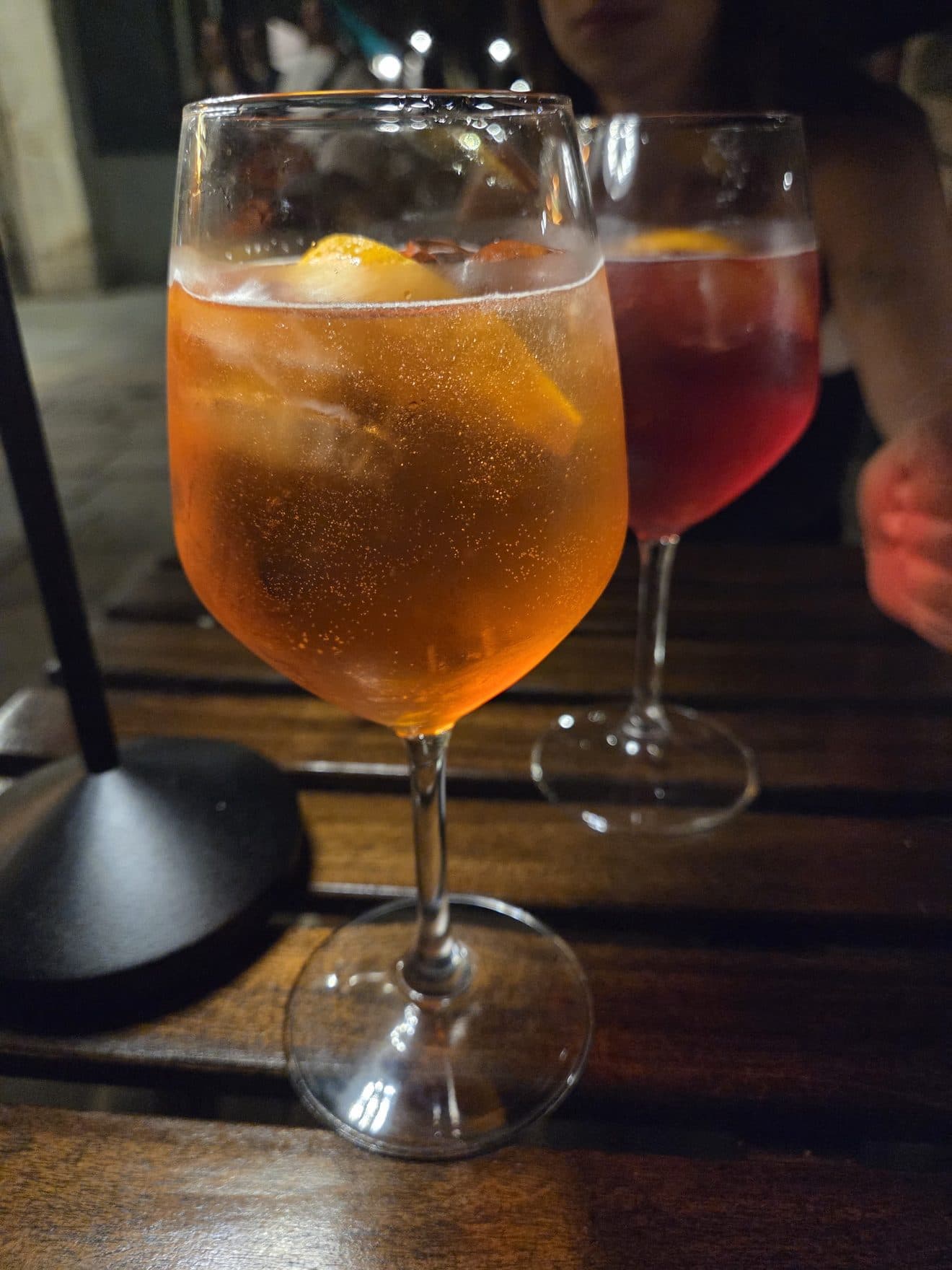 Two spritzes, one orange and one red, on a wooden table at night